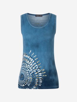 Lächelnde Frau in lässiger Haltung in dem Yoga Top Peace OM in blau. Man sieht einen schönen Mandala Print an der Hüfte mit Golddruck, der im Licht glitzert. Fair und nachhaltig von The Spirit of OM hergestellt. Mit Rosenquarz. 